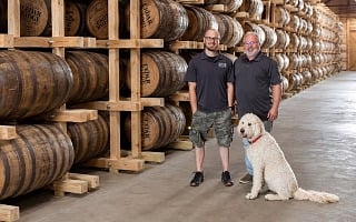 A father and son with their dog among the whiskey barrels in the rickhouse at Cedar Ridge Distillery in Iowa