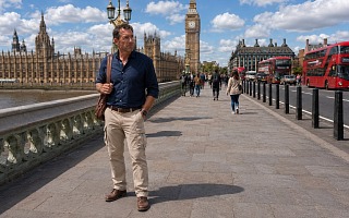 A man in well-fitted beige cargo pants and leather shoes walking across Westminster Bridge with Big Ben and the Houses of Parliament in the background