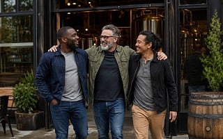 Three friends laughing together outside a brewery on a guys trip
