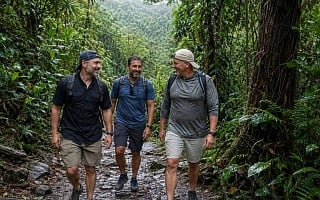 Three men hiking a wet rocky trail through the El Yunque rainforest in Puerto Rico