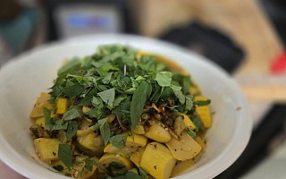 Cooked yellow summer squash and caramelized garlic in a white bowl under a heap of freshly picked basil