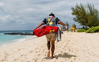 A golfer walks a Barbados beach carrying the red Mount Gay 1703 Devereux Golf bag and checkered towel