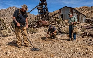 Three guys metal detecting and digging for treasure at an abandoned desert gold mine with a rusted headframe