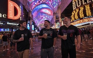 Three guys laughing on Fremont Street under the canopy holding drinks during a Vegas guys trip