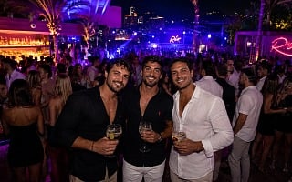 Three guys at an upscale Río nightclub in South America with cocktails, palm trees, and a packed crowd at night