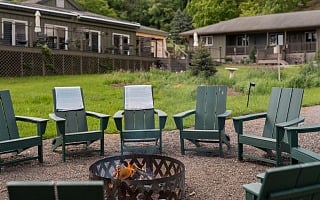 Fire pit ringed with green Adirondack chairs at Hemlock, the adult summer camp resort in the Catskills
