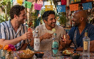 Three friends celebrating Cinco de Mayo with tequila, mezcal, and Fluere cocktails at an outdoor cantina under papel picado banners