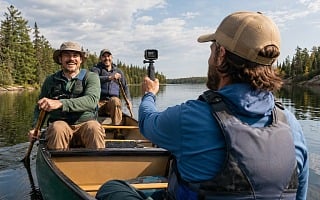 Three guys in a canoe on a northwoods lake, one filming the others with an action camera on a grip