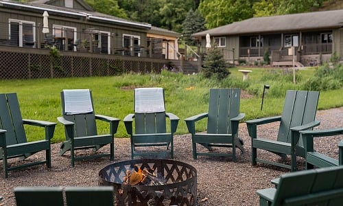 Fire pit ringed with green Adirondack chairs at Hemlock, the adult summer camp resort in the Catskills