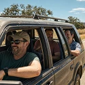Group of men laughing in a dusty SUV with the windows down on a summer road trip through the Texas Hill Country