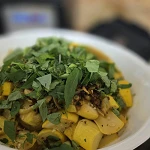 Cooked yellow summer squash and caramelized garlic in a white bowl under a heap of freshly picked basil