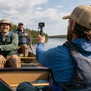 Three guys in a canoe on a northwoods lake, one filming the others with an action camera on a grip