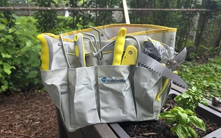 Yesker 10-piece garden tool set loaded in its gray and yellow tool bag on a raised bed next to a basil plant