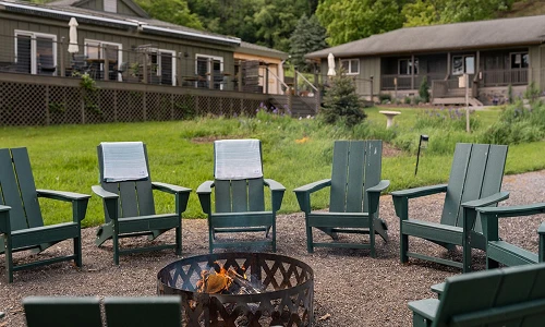 Fire pit ringed with green Adirondack chairs at Hemlock, the adult summer camp resort in the Catskills